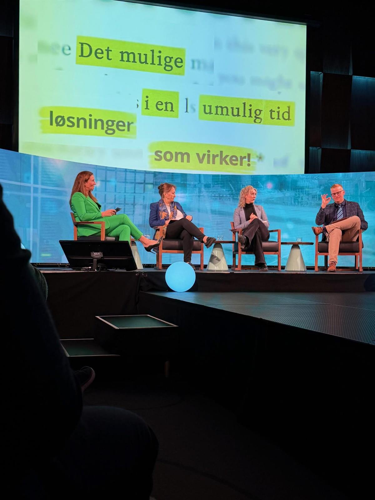 Fire mennesker på en scene med en stor skjerm bak dem - Klikk for stort bilde